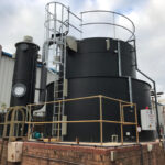 Black chemical tank with ladder access to the side on top of brick structure