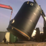 Two black chemical storage tank being installed using a crane