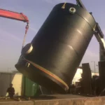 Two black chemical storage tanks being installed using a crane