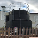 Black tank outside a warehouse with a wooden fence in front of it