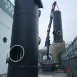 Two black chemical storage tank being installed using a crane