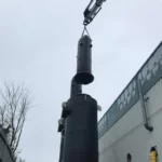 Black chemical storage tank being installed using a crane