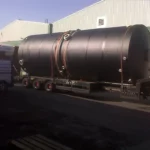 Black chemical storage tank on the back of a truck on a bed outside a warehouse